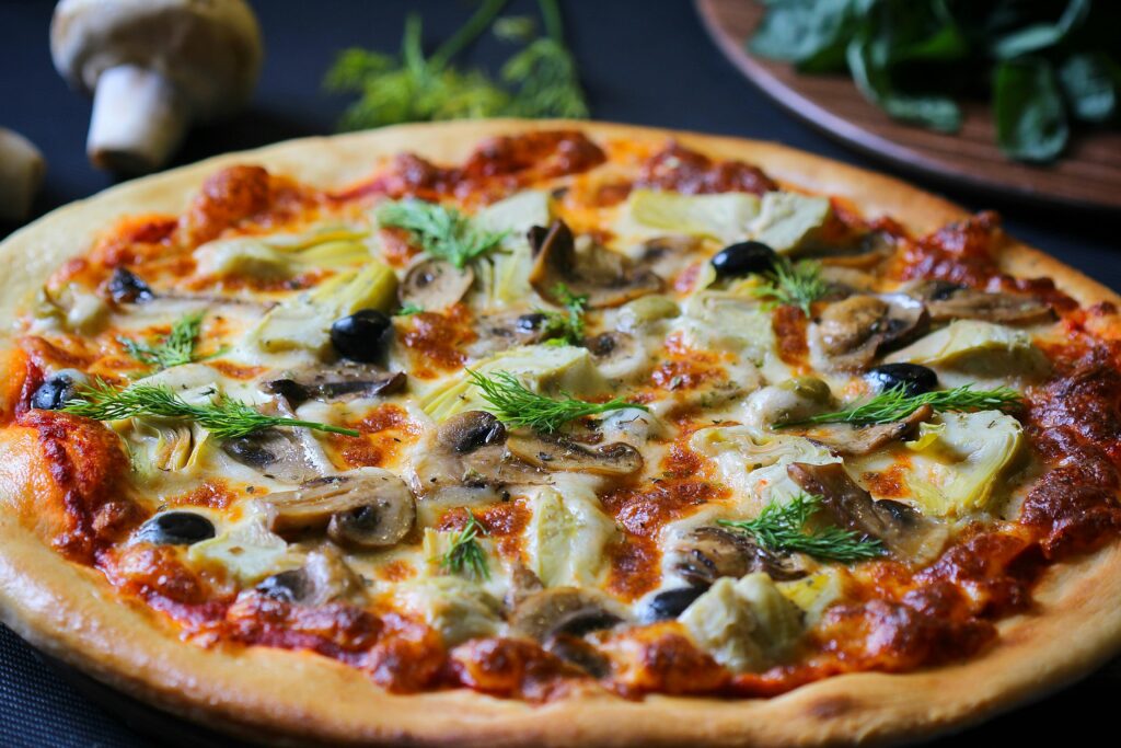 Vegetarian pizza topped with artichoke hearts, sliced mushrooms, black olives, and fresh dill on tomato sauce base.