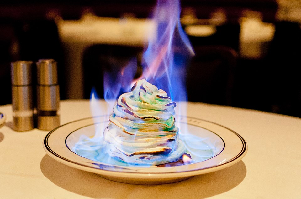 Baked Alaska engulfed in blue flames on a restaurant plate.