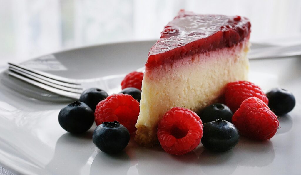 Slice of cheesecake with raspberry topping surrounded by fresh berries.