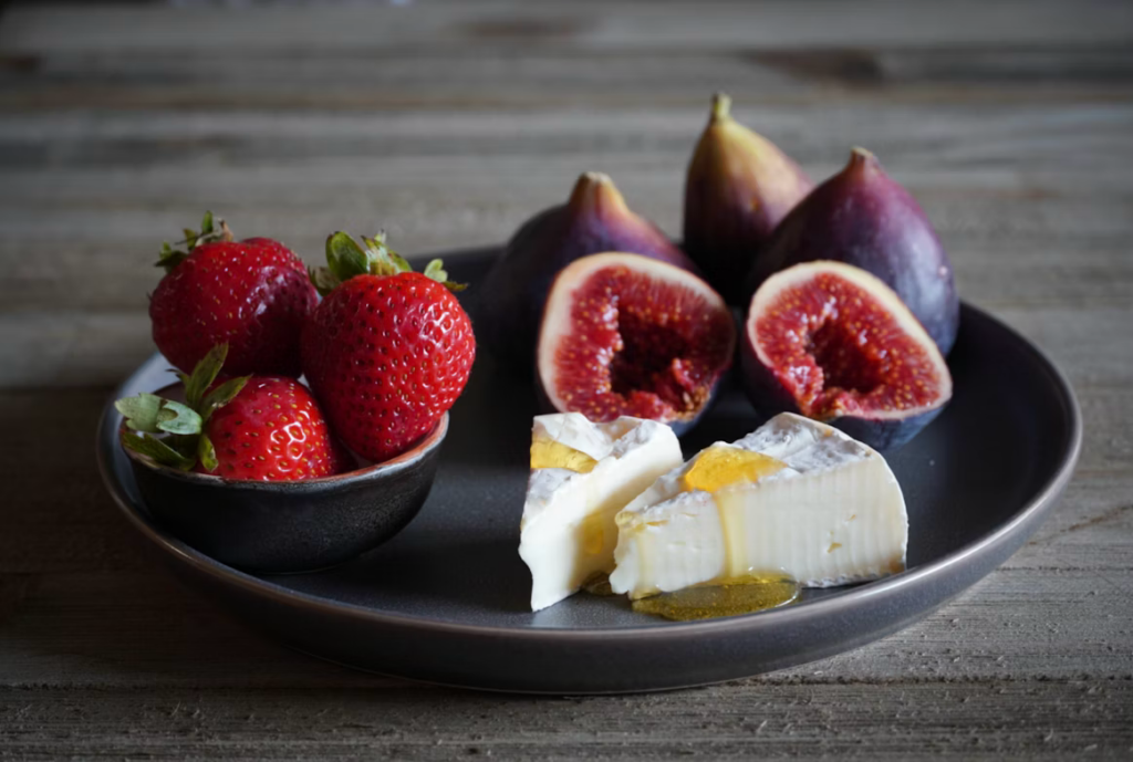 Fresh figs, strawberries, and brie cheese arranged on a dark ceramic plate.