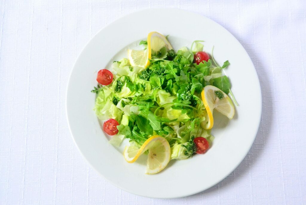 Fresh green salad with cherry tomatoes, broccoli florets, and lemon slices on a white plate.