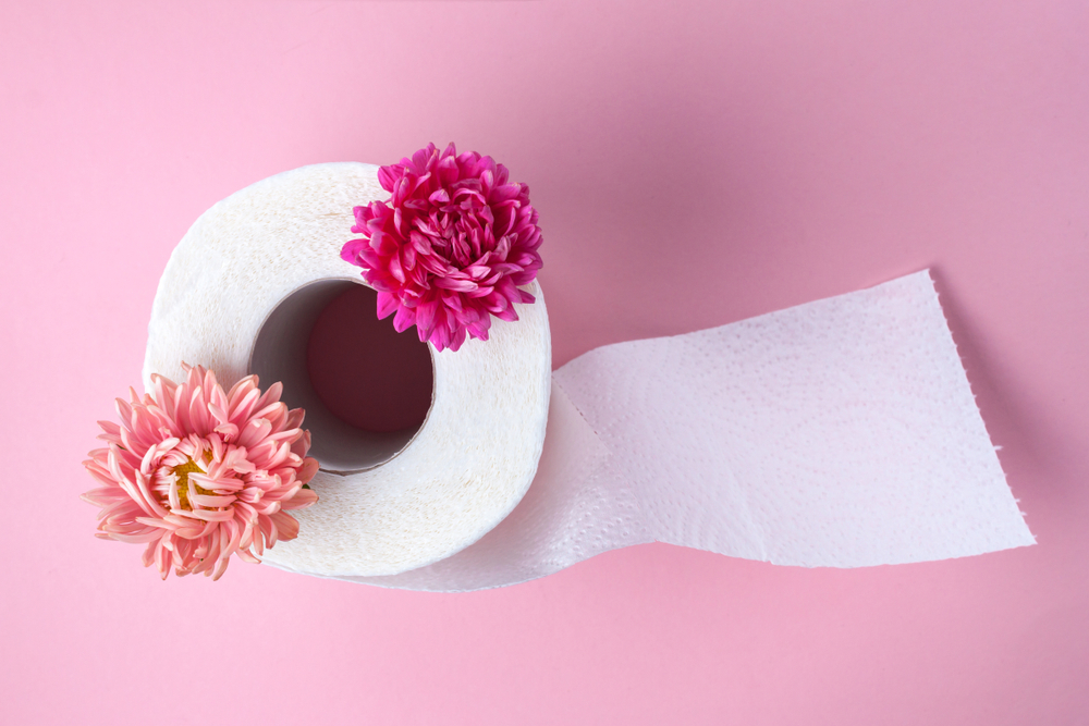Scented toilet paper roll and a pink flowers on a pink background. Toilet paper with a smell. Hygiene