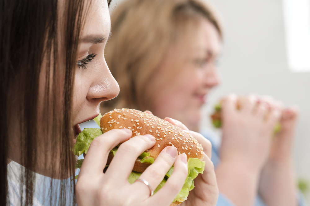 Two girls, slim and fat, blonde and brunette, eat hamburgers. On a white background, the theme of diet and proper nutrition, choice and opposition.