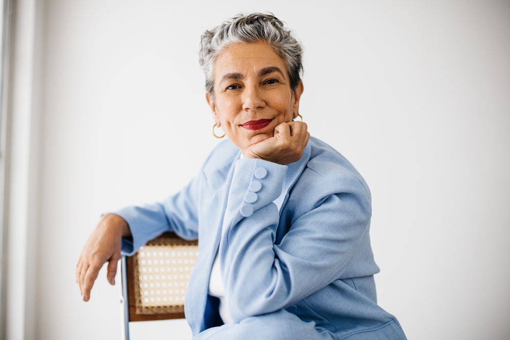 Female professional looking at the camera in her office. Dressed in a professional suit and grey hair, she expresses her confidence and empowerment as an experienced and accomplished business woman.