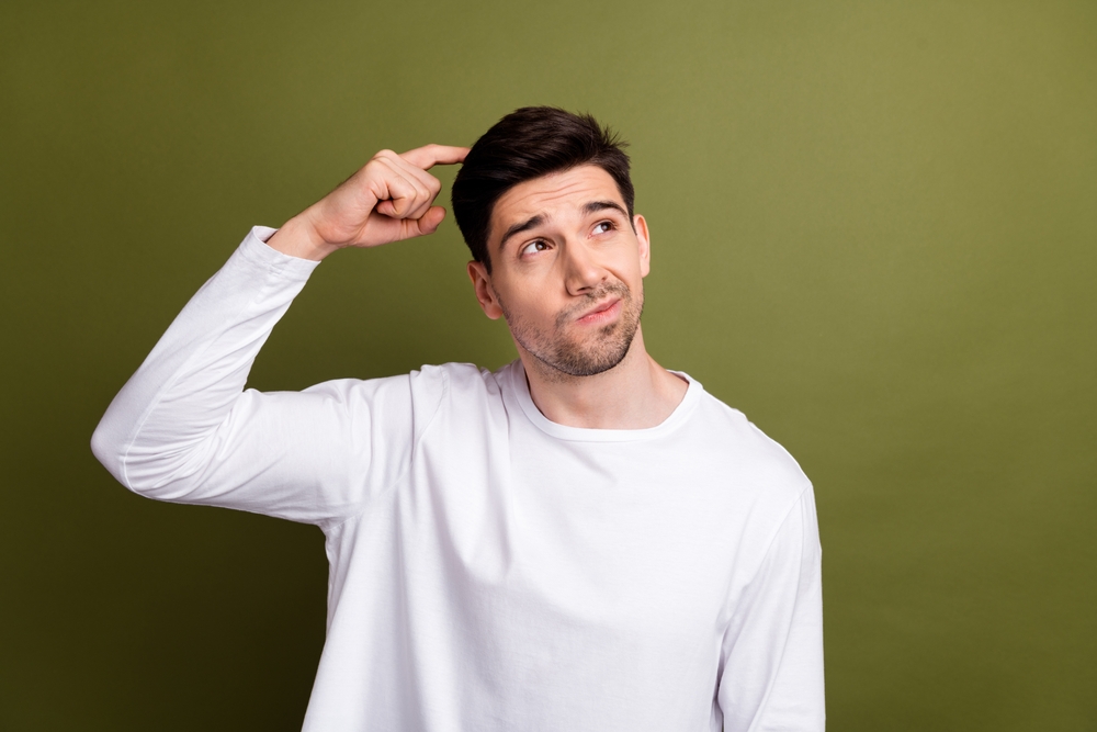Photo of young stupid minded guy scratching head when someone asks him what time is now looks novelty isolated on khaki color background