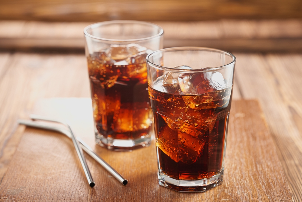 Two glasses of iced cola on a wooden table with metal straws.