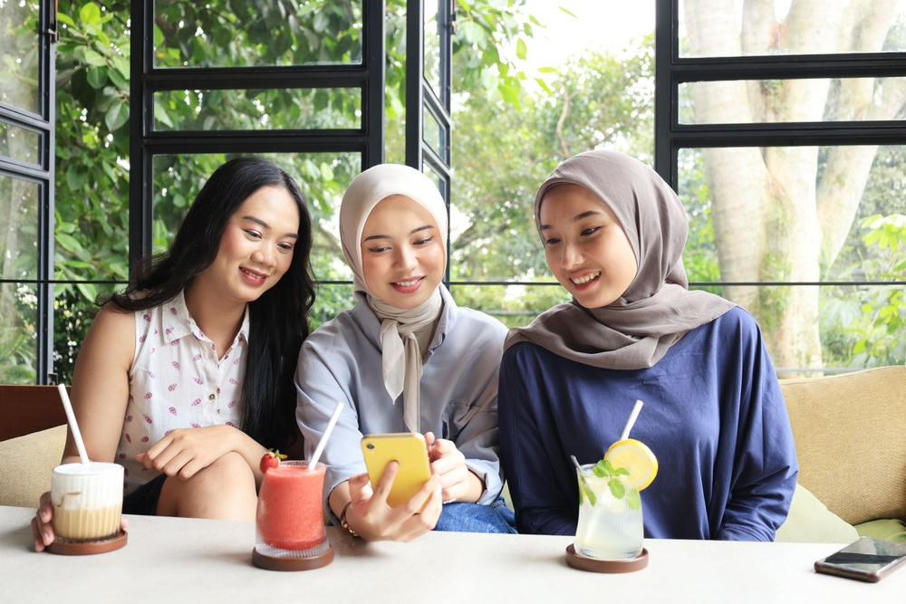 Group of Cheerful and Pretty Asian Female Friends are Enjoying Eating food, Drinking, and Hanging Out at a Restaurant or Cafe with Green Plant Outdoor, Making Trend Challenge