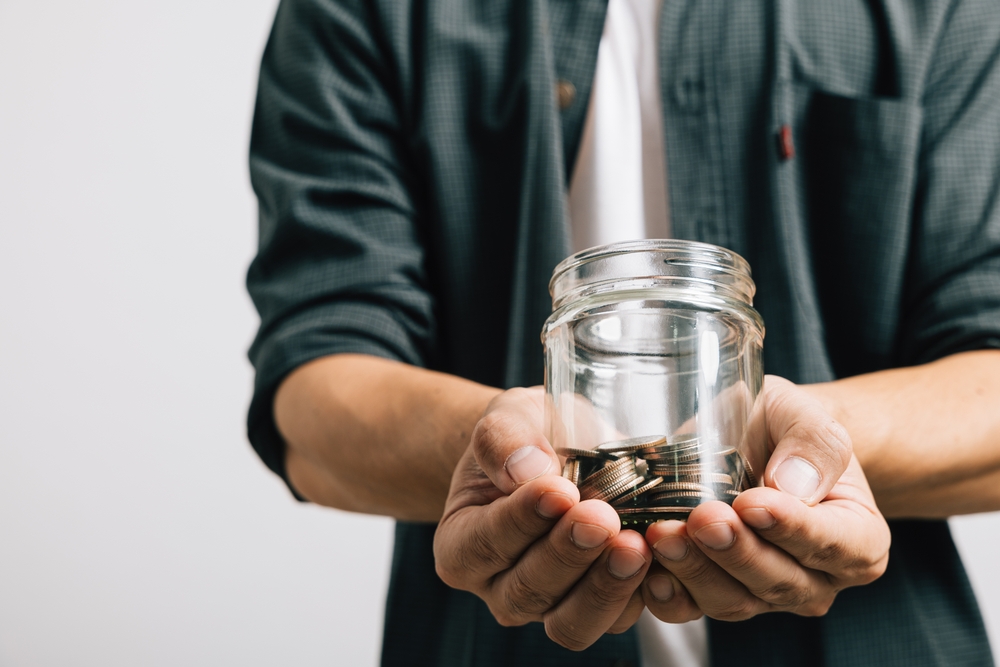 Close up hand of businessman holding a jar full of coins and the coins are in his palm studio shot isolated white background, Money saving and investing or donate money concept
