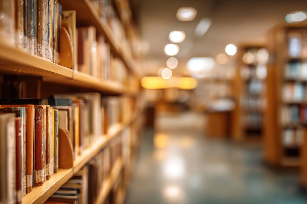 Rows of bookshelves filled with numerous books line a library aisle, creating a warm and inviting atmosphere. The background is softly blurred, showcasing th...