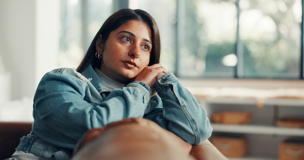 Thinking, mental health and woman in home with sofa, reflection or memory of past trauma. Grief, flashback and Indian female in living room with couch, anxiety trigger or fatigue in emotional thought