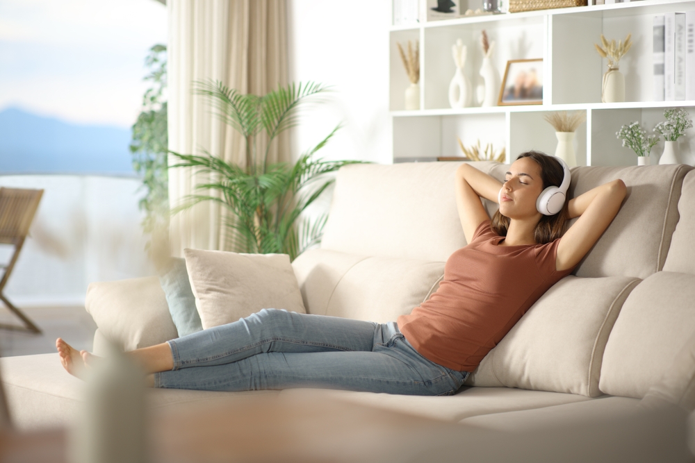 Woman listening music from headphone relaxing sitting on comfortable sofa at home