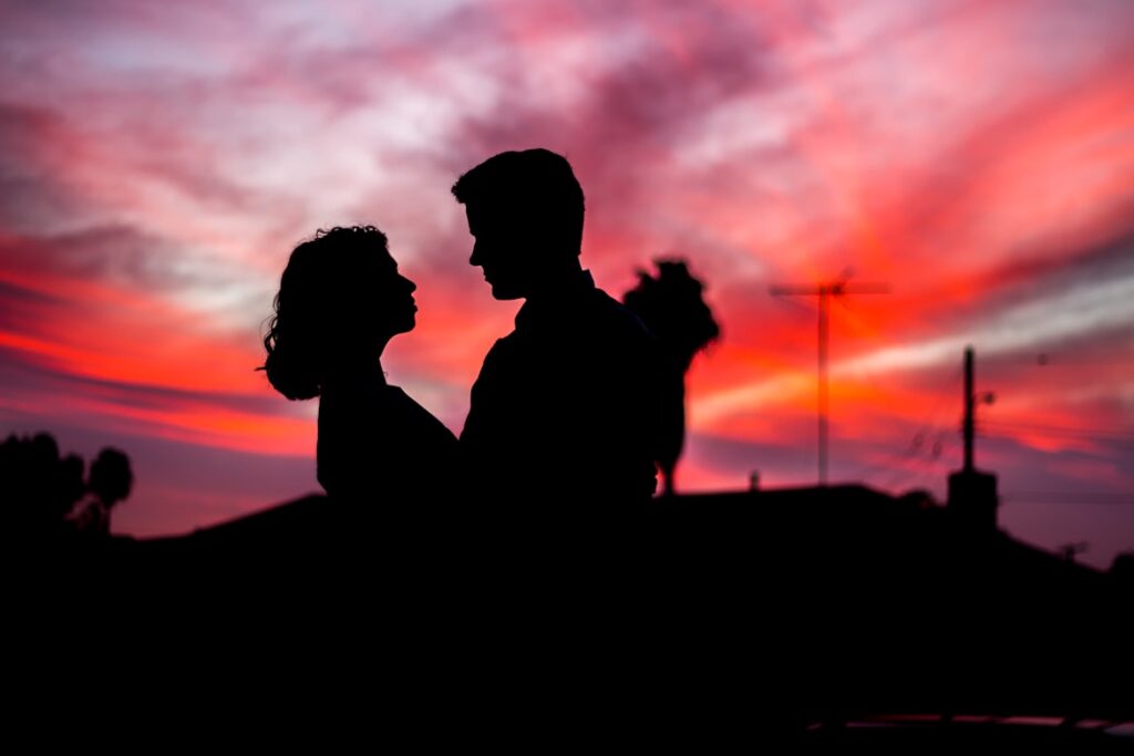 Silhouette of a couple facing each other against a vibrant pink and orange sunset sky.