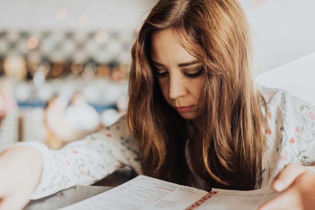 Woman with long auburn hair reads a book while lying down, soft light in the background.