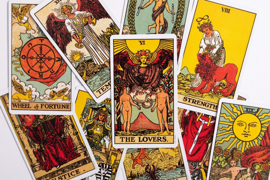 A spread of colorful tarot cards on a white surface, with The Lovers card prominently displayed in the center alongside Wheel of Fortune, Strength, and several others.