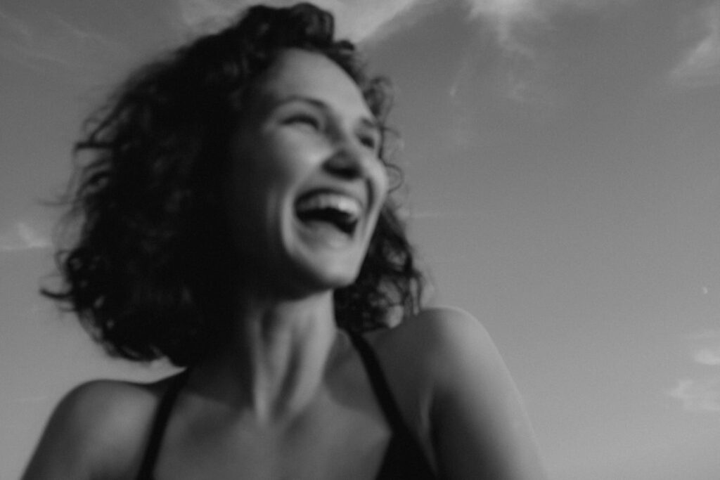 Black and white photo of a woman with curly hair laughing freely, her face tilted toward the sky.