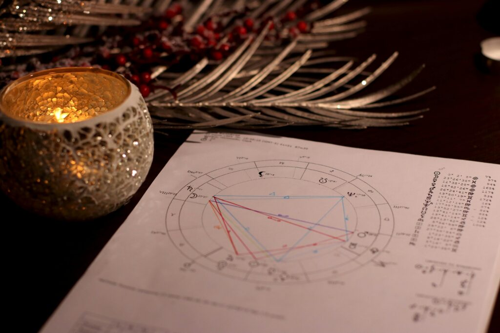 A printed astrology birth chart lies on a table beside a glowing candle and silver holiday decorations.