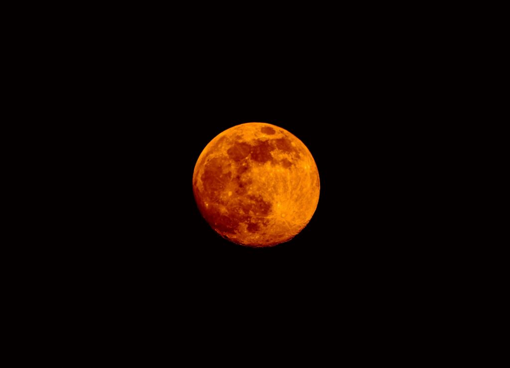 A full moon glowing deep orange against a pitch-black sky, its craters and surface details clearly visible through the warm amber tones.