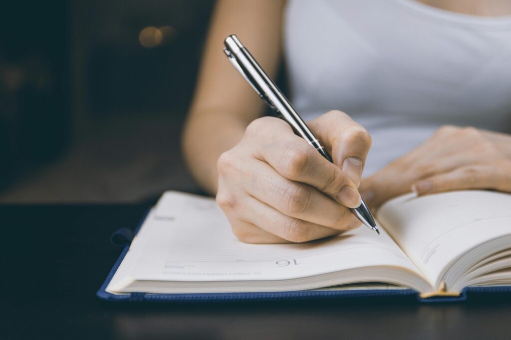 Close-up of a woman's hand writing in an open notebook with a silver pen.