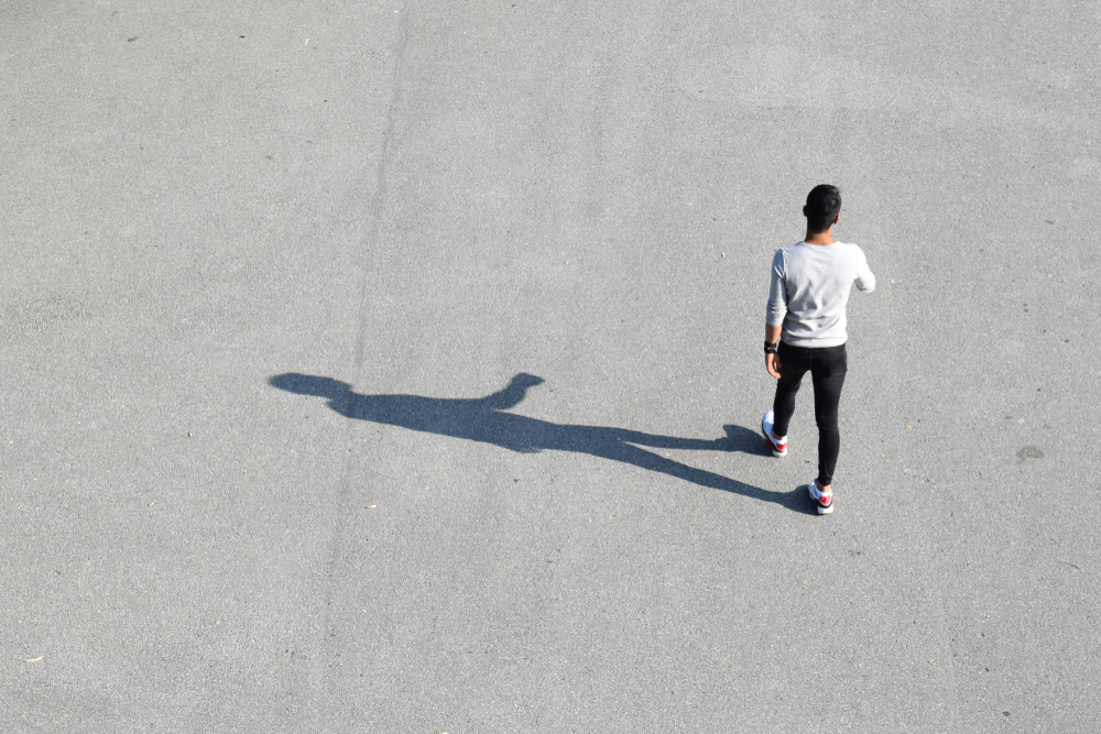 VIENNA, AUSTRIA - AUGUST 28, 2018: Walking young man and his shadow on asphalt surface, as seen from a higher point