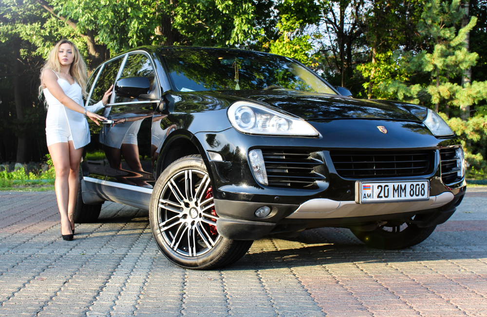 Yerevan, Armenia - 22 August 2018.
Black luxury car Porsche Cayenne and pretty model under summer sun.