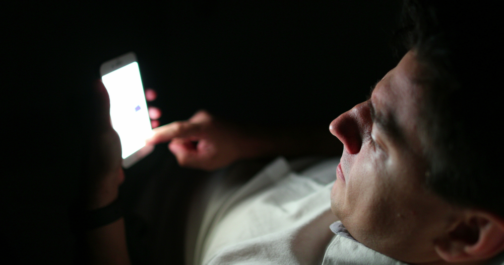 Man holding smartphone device at night in the dark screen light glowing person scrolling