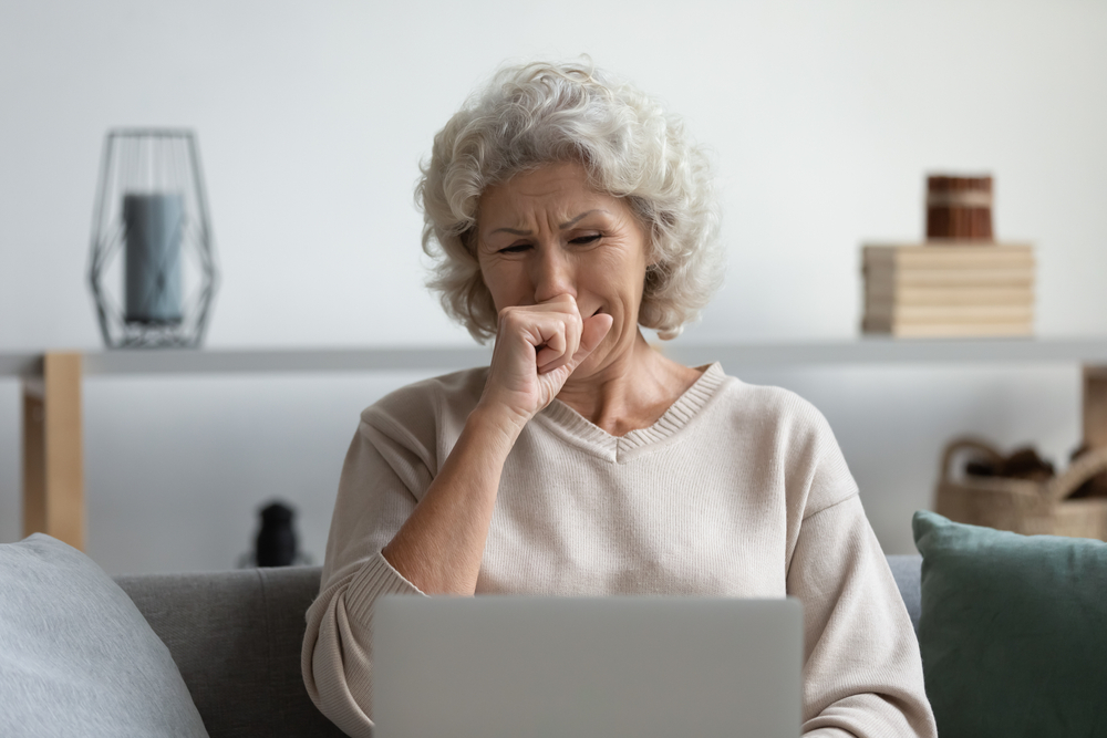 Front view depressed senior older woman crying, looking at computer screen. Stressed worried middle aged mature grandmother grieving, received bad message notification, sitting alone at home.