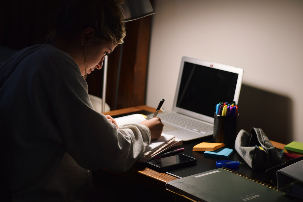 Young teenage girl student studying late at night in her room