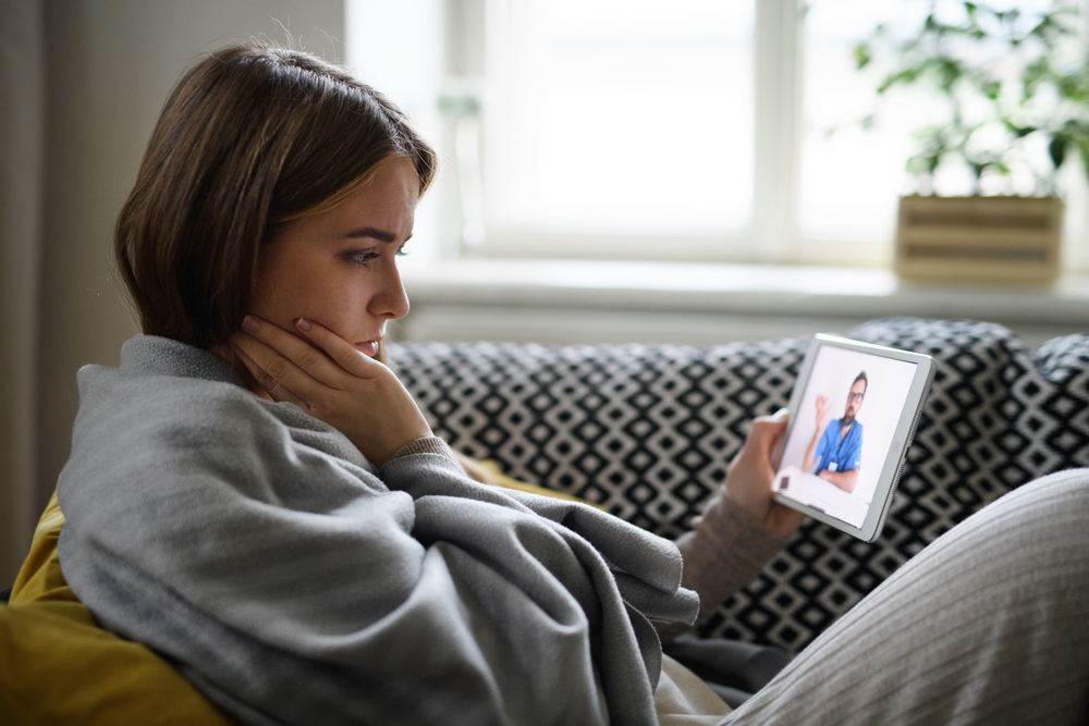 Young woman having video call with doctor on tablet at home, online consultation concept.