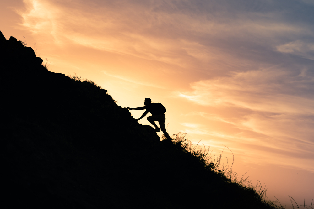 Young man climbing up to top of mountain. Self improvement and motivational goals concept. 