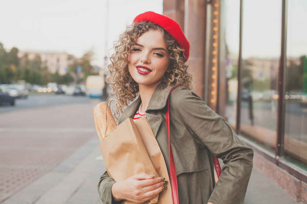 Beautiful young woman walking along city street. Portrait of nice young woman wearing a trench coat, looking at camera and smiling