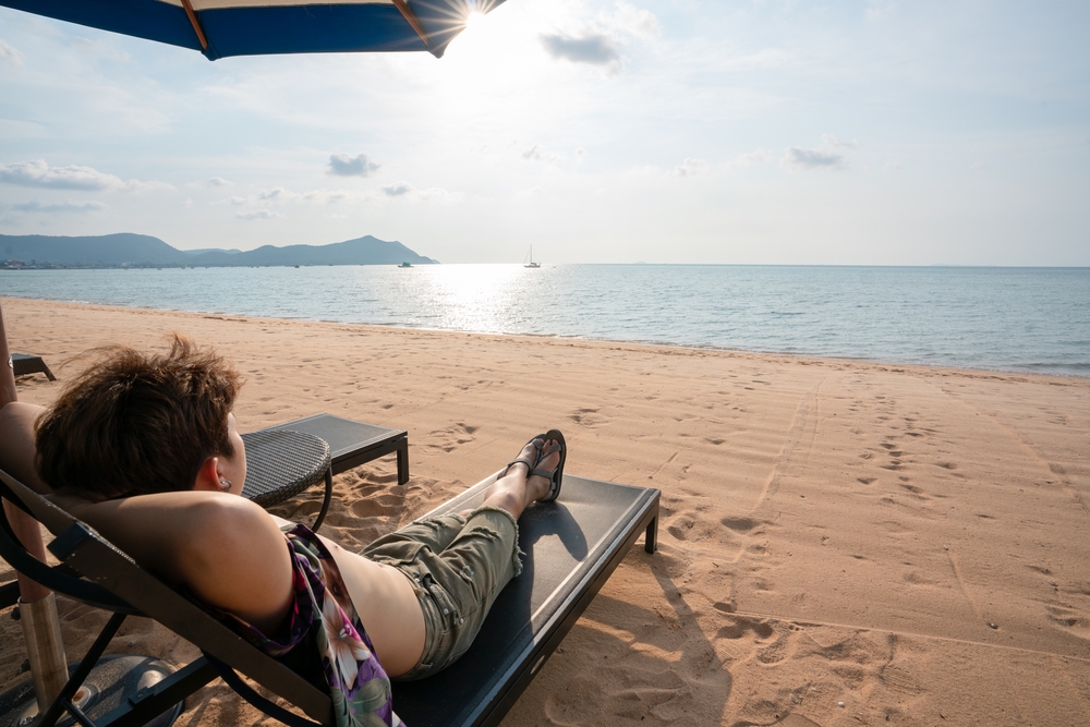 Happy man relaxing on sand beach during summer vacations. Young man enjoying sunny on the tropical beach.