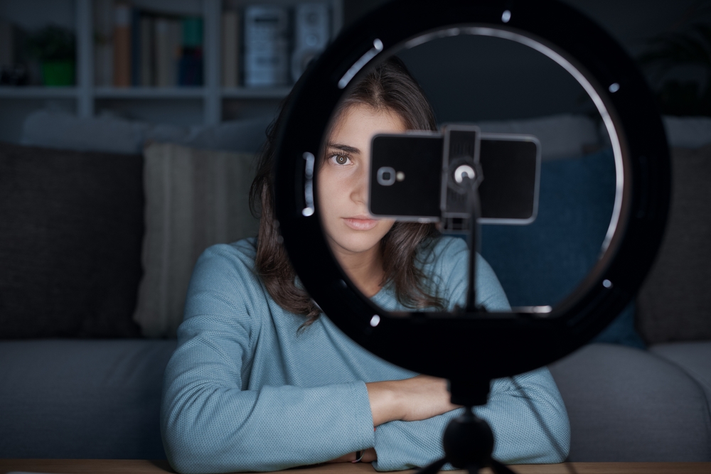 Influencer girl creating videos for social media at home, she is using a smartphone and a ring light