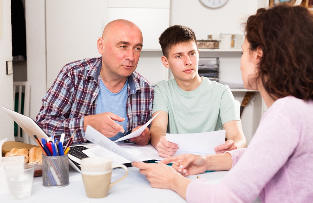 Young woman with her husband and teen son calculating domestic budget at table ..