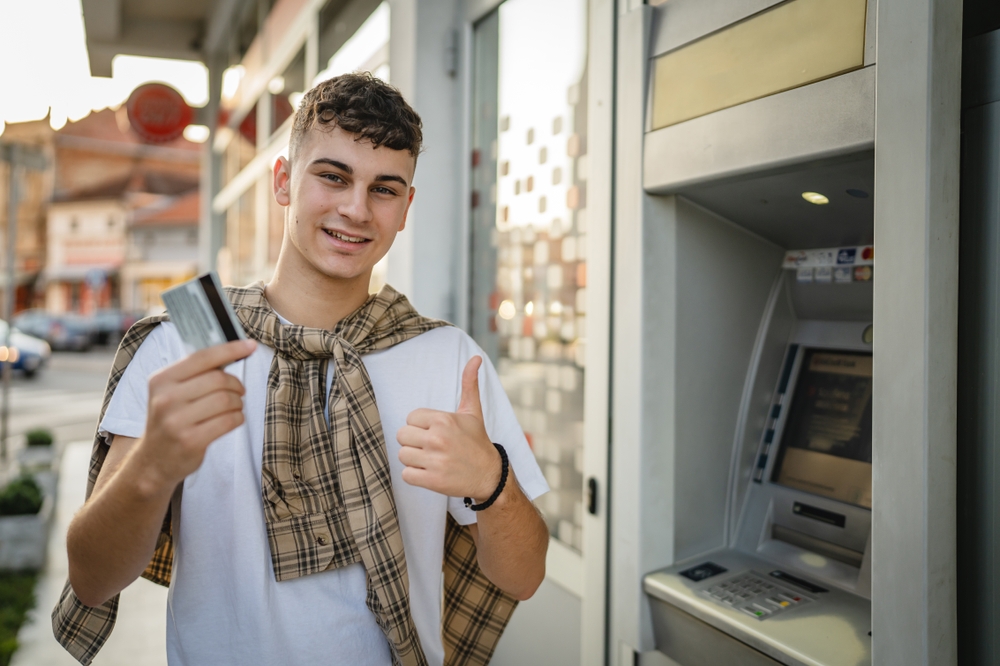 portrait of teenager man stand in front of bank ATM hold credit card
