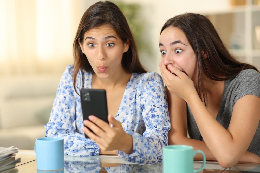Two amazed women checking smart phone at home