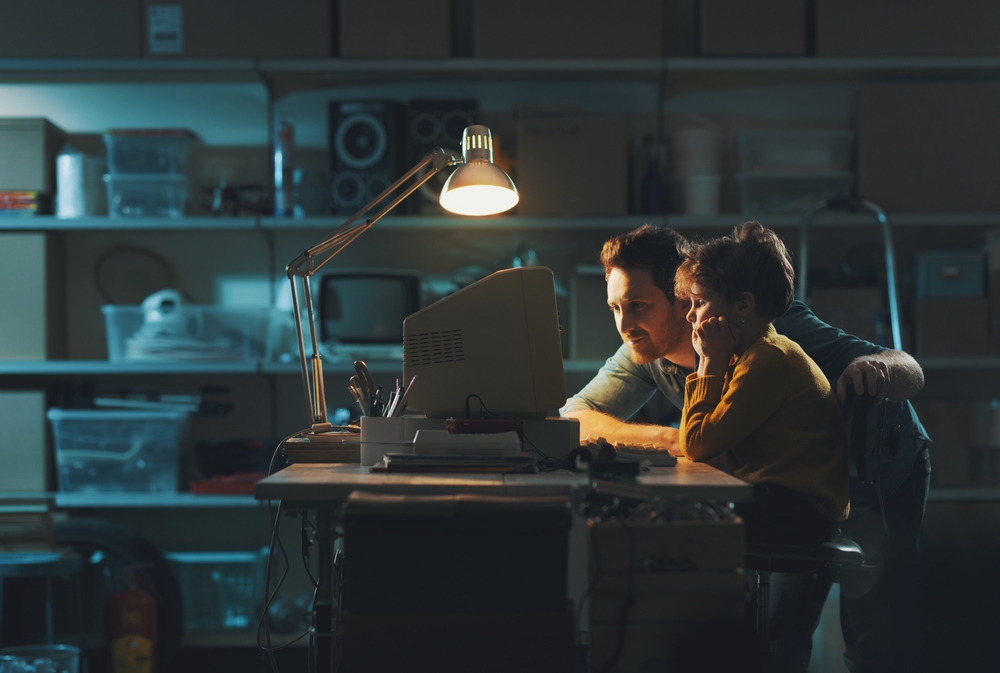 Young caring father and boy in the garage, they are using an old computer and playing together, family and togetherness concept