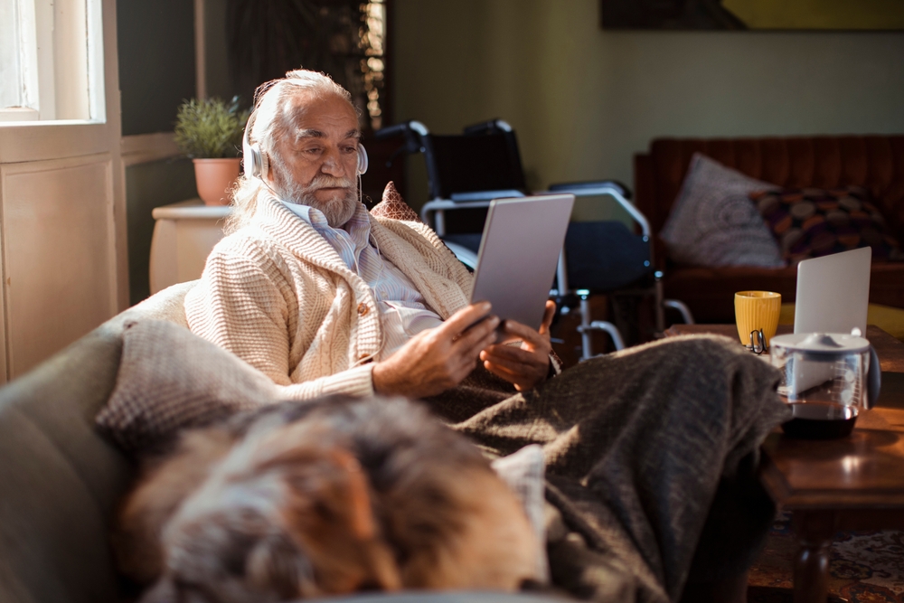 Senior man using tablet with headphones on home sofa