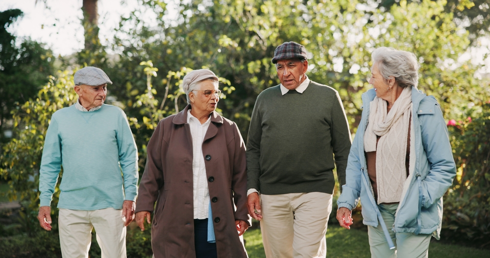 Senior people, walking and bonding in retirement home as pensioners for activity, together or relax. Group, elderly care and friends for outdoor, garden or backyard in nursing village or community