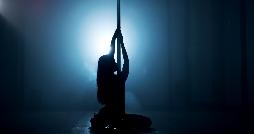 Woman, dancing or pole with spotlight for silhouette, tease performance or sexy movement in nightclub. Person, dark background or girl in stage routine for seduction, strip or party entertainment