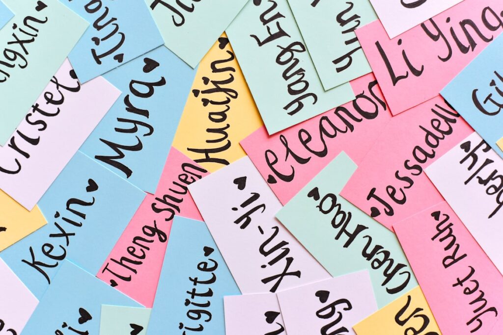 Scattered colorful paper cards in pastel pink, blue, yellow, and mint green, covered with handwritten calligraphy names including Kexin, Myra, Huailin, Eleanor, Li Ying, and Jessadeli.