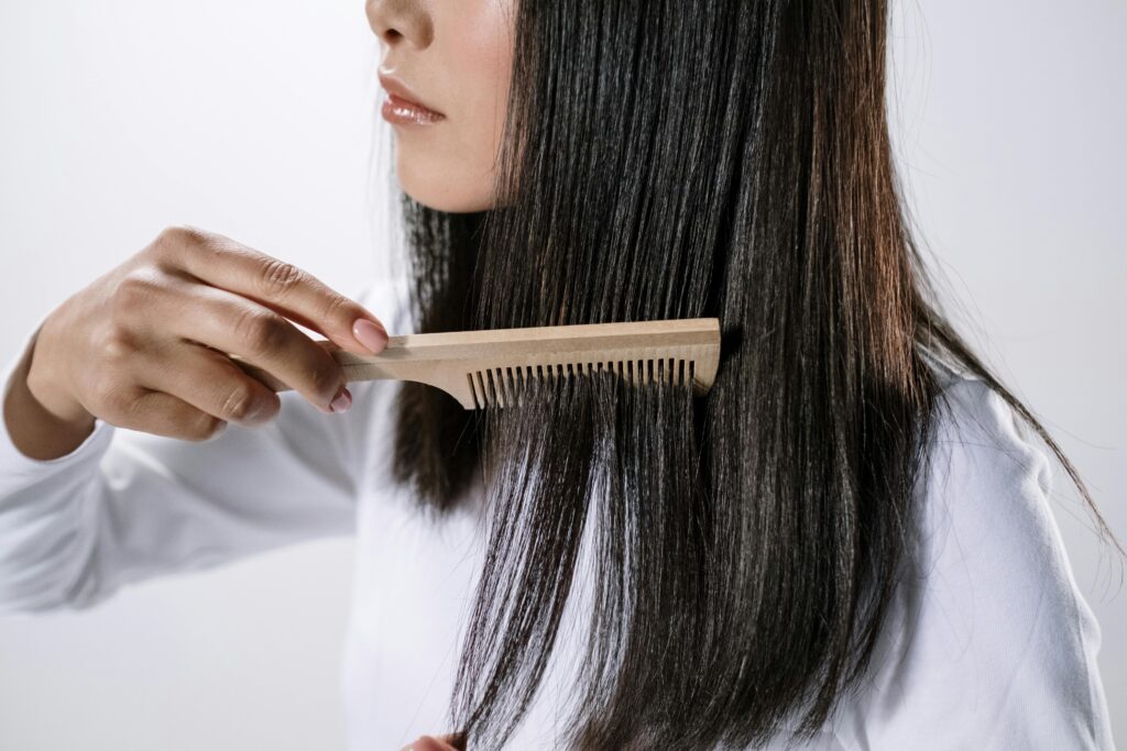 Woman combing her long, straight dark hair with a wooden comb against a white background.