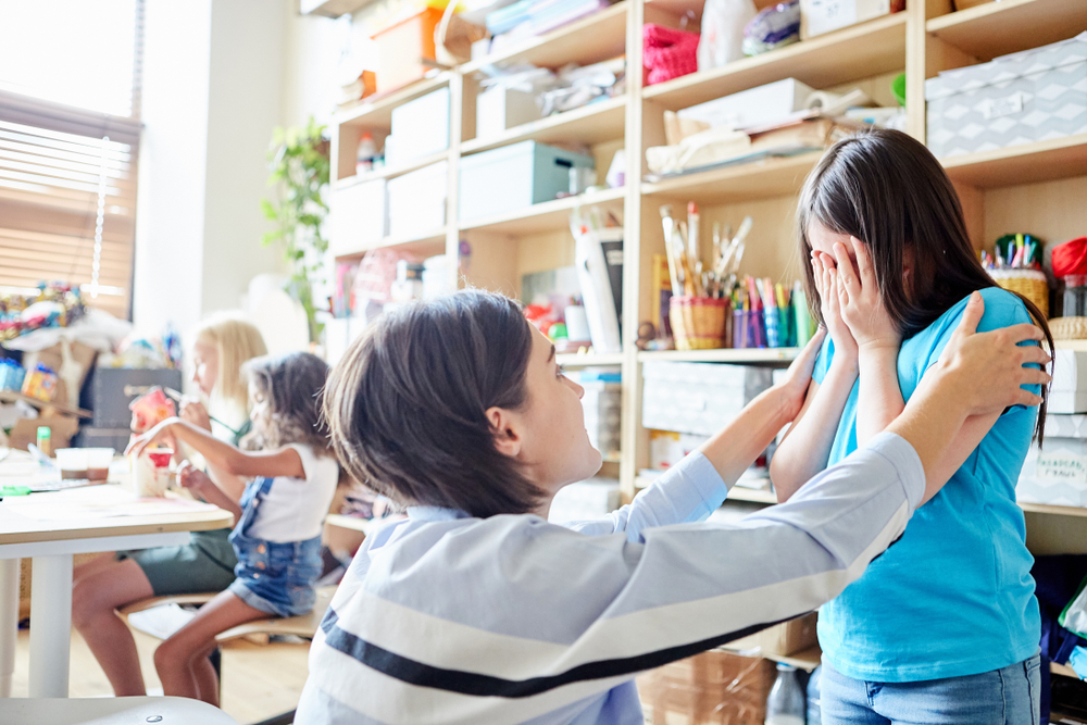 Side view of young female comforting crying girl during lesson in art school