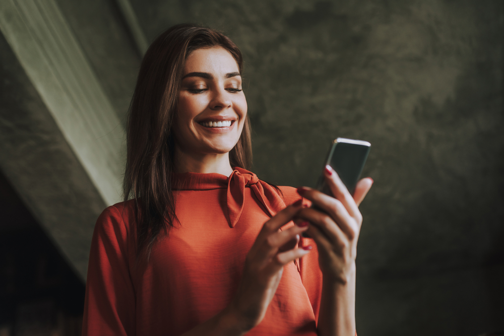 Concept of success and well-being. Close up low angle portrait of smiling business lady reading messages on mobile phone