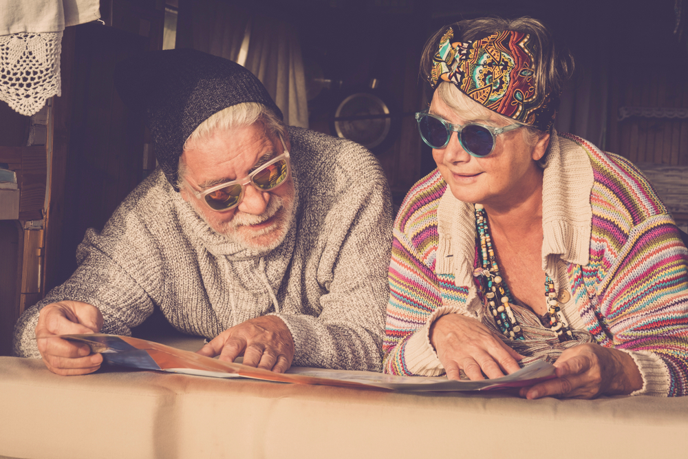 Adults mature couple of caucasian people hippy style planning on the map the next step of van life vacation - cheerful happy man and woman retired and living a new life - colors and enjoying