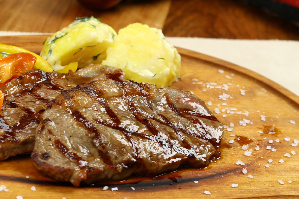 Striped rib-eye steaks with vegetables and potato on wooden board