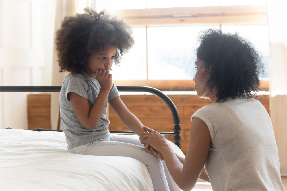 Caring worried african american mother holding hand of sad little multiracial daughter talking giving support and comfort black mom foster parent consoling small kid being bullied sit on bed at home