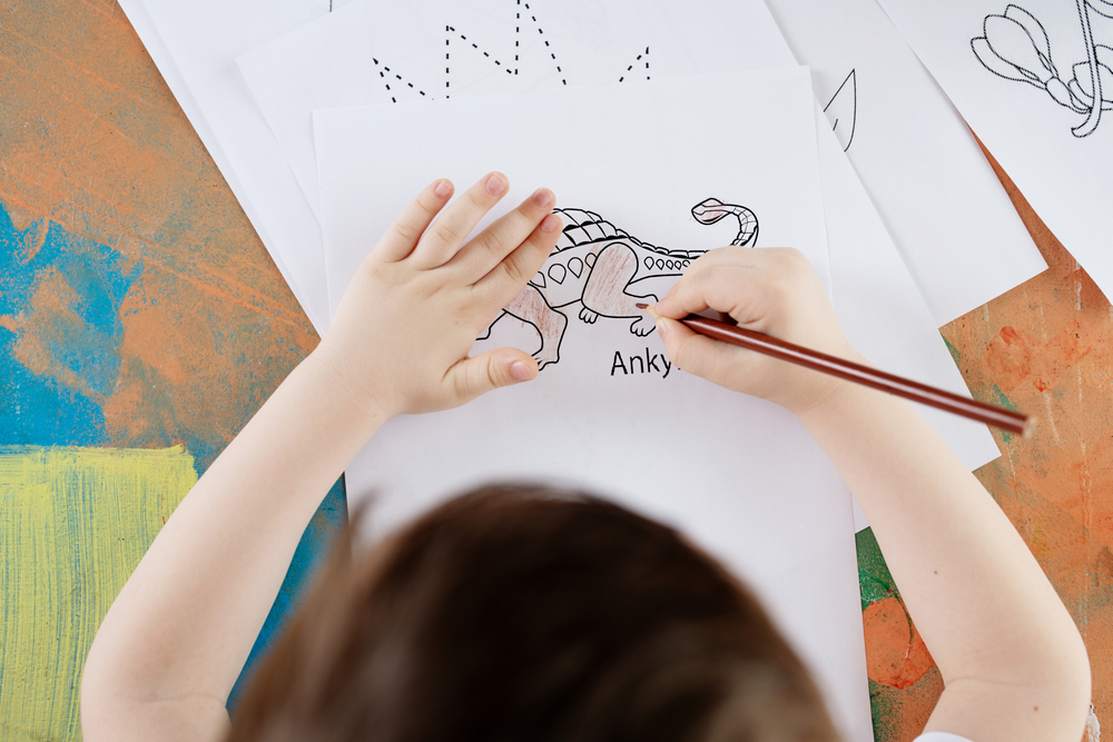 Small child coloring a dinosaur on printed coloring sheet; overh