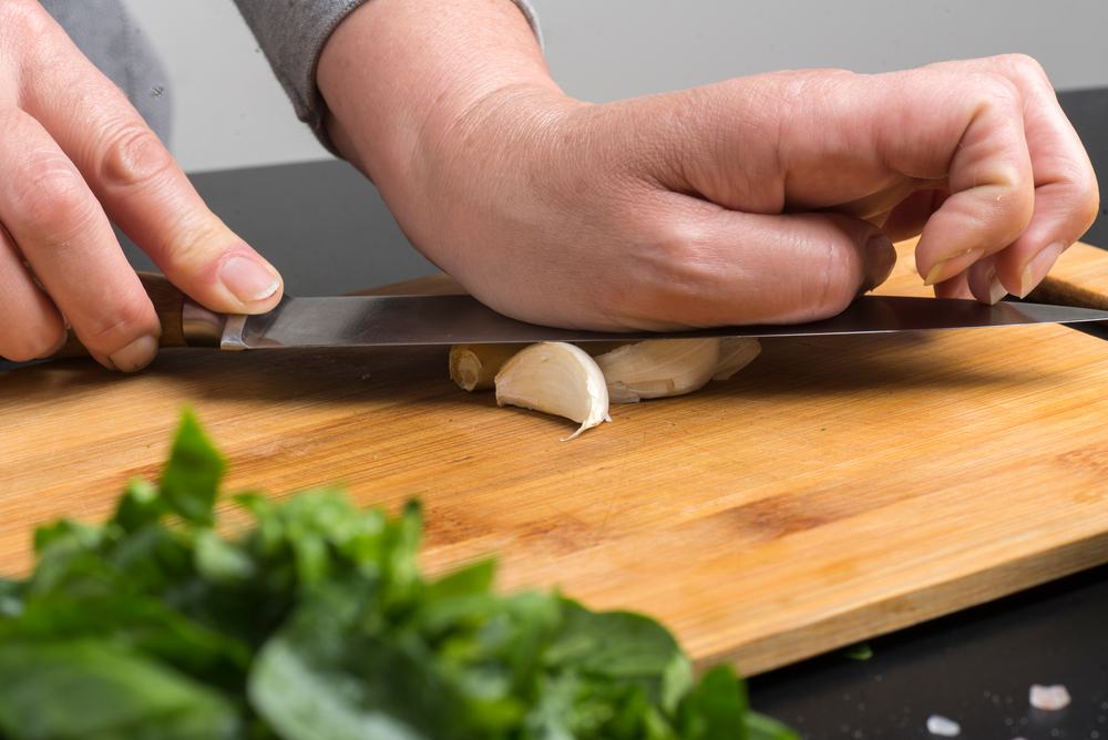 chef's hands crush the garlic with  knife on the board