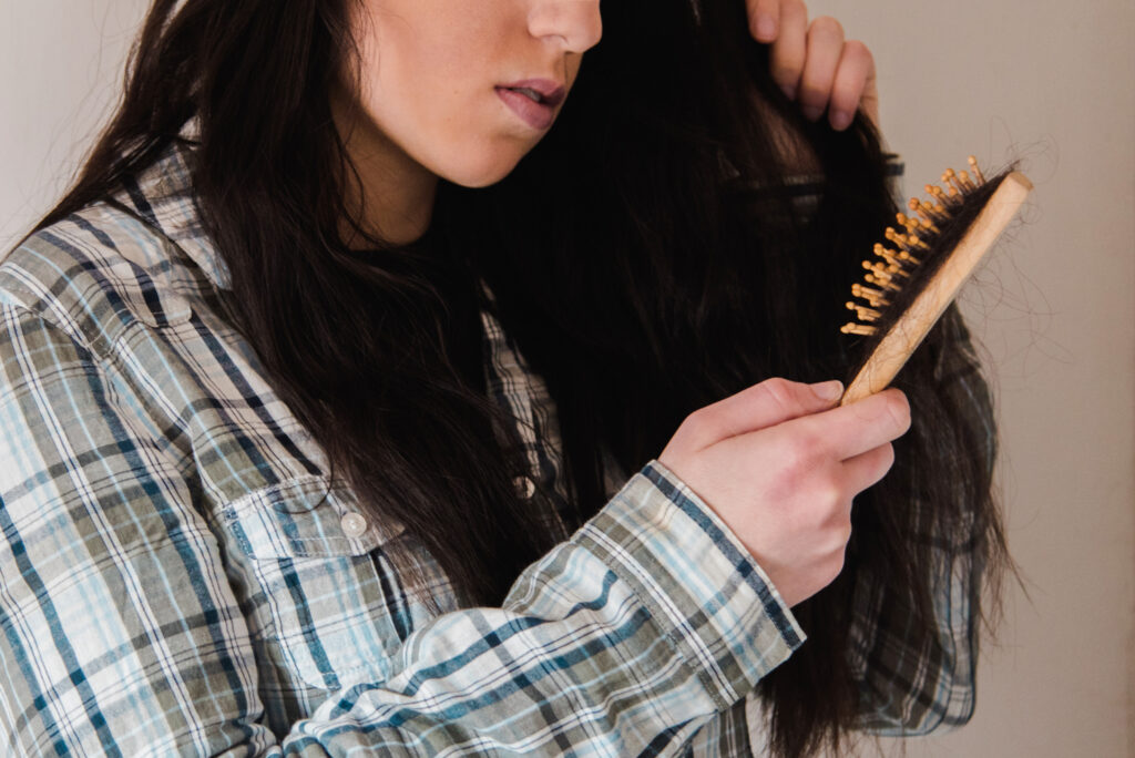 Young brunette girl combing her long black hair, looks frustrated