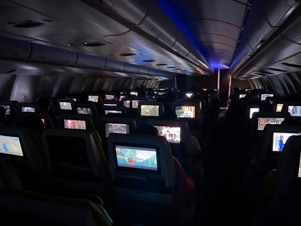 Amsterdam Netherlands 21 04 202 Interior os airplane economy class at night with light on screens monitor front of sitting dark rows blue indoor technology streaming service aeroplane transportation